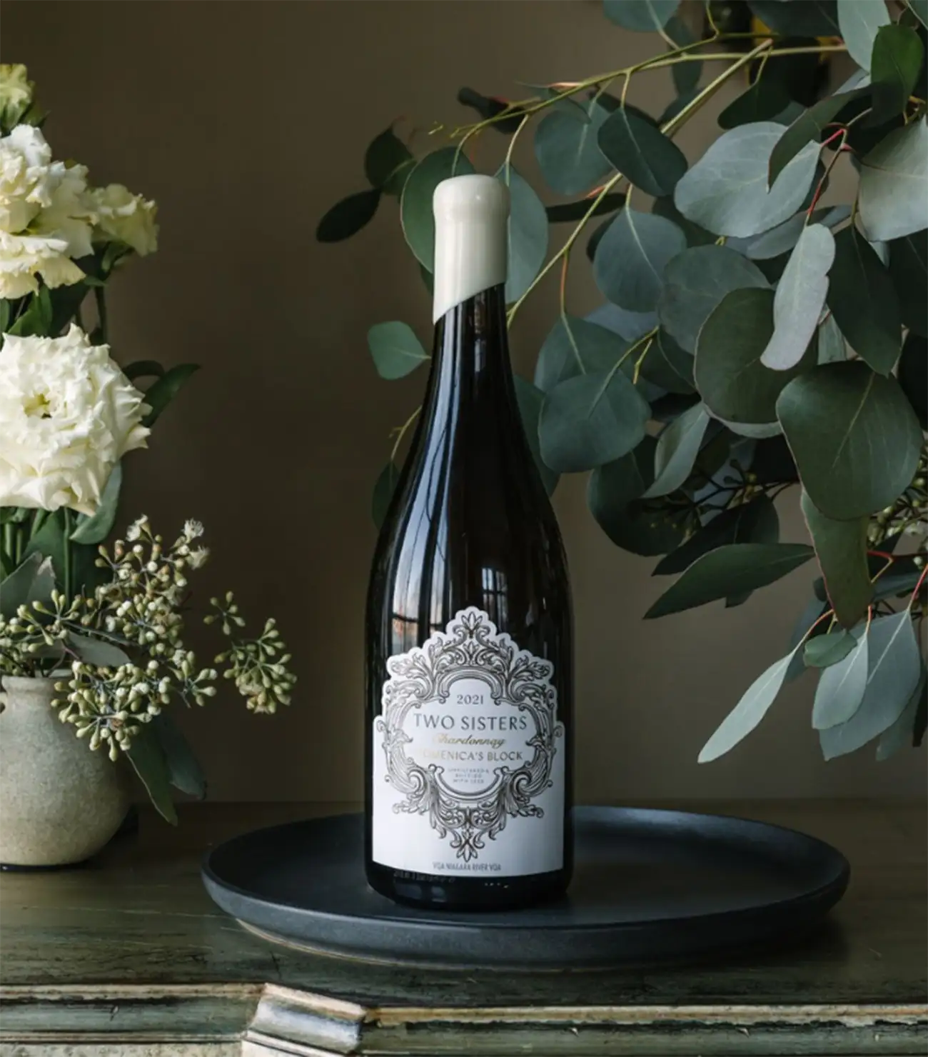 Two Sisters Vineyards Wine on a tray beside a floral arrangement.