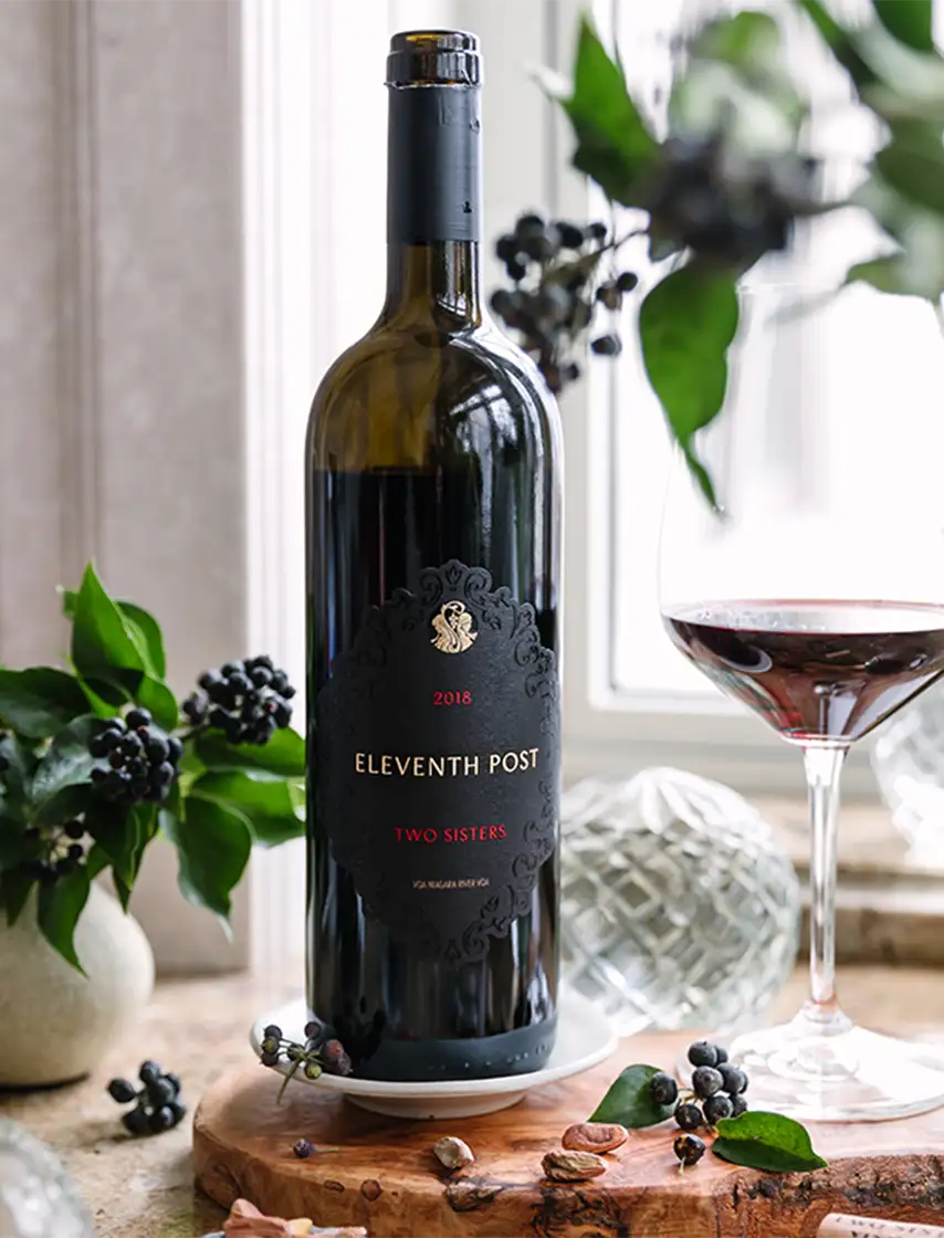 Two Sisters Vineyards Wine bottle and wine glass beside each other.