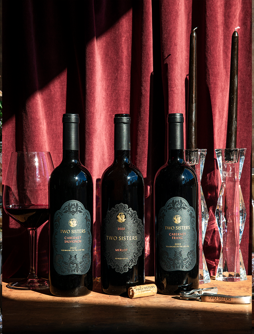 Two Sisters Vineyards Wine bottle and wine glass beside each other.